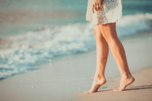 Close-up of a woman’s legs walking on the sandy shoreline of Hiriketiya Beach, Sri Lanka, during sunrise.