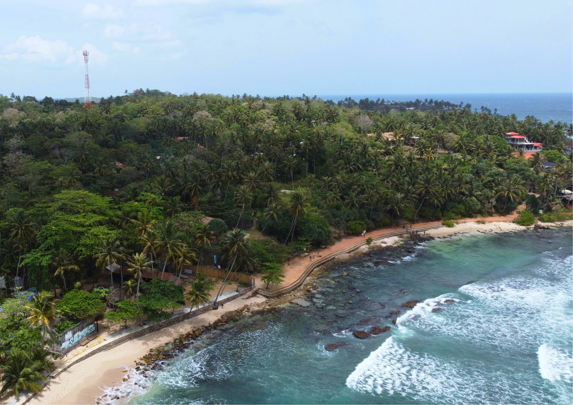 Aerial drone view of the lush, palm-fringed headlands of Hiriketiya Bay, showcasing the intimate "jungle-meets-sea" geography that distinguishes it from Mirissa.